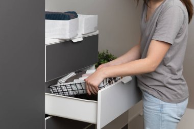 Giysilerin dikey depolanması. Kadınlar kıyafetleri modern bir yatak odasında düzenler. Kadınlar sepet oda temizleme konseptinde kıyafet sıralıyorlar..
