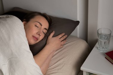 Genç kadınlar geceleri huzurlu bir gülümsemeyle yatakta uyuyorlar. Mutlu rüyalar ve iyi uykular..