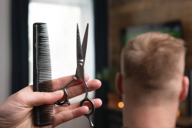 Tarağı ve makası önde tut. Televizyonun karşısında kocanın saçını kesiyorsun..