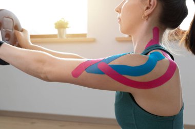 Genç ve zinde kadınlar, güneşli bir günde omzunda elastik terapi bandıyla egzersiz yapıyorlar. Kineziyoloji fizyoterapisi.