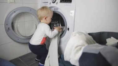 Ev işleri yapan iki yaşında bir çocuk. Çamaşır makinesi yükleniyor.