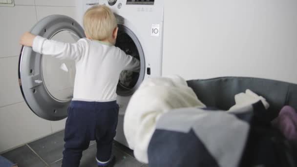 Zweijähriges Kind bei der Hausarbeit. Waschmaschine beladen.