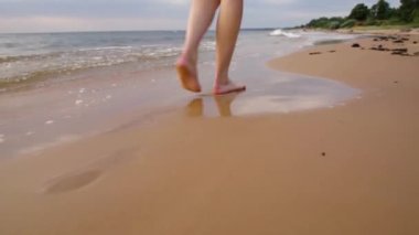 Kumsalda yürüyen bir kadın kumların üzerinde ayak izleri bırakıyor.