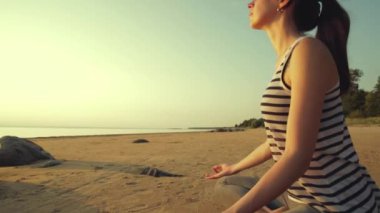 Lotus pozisyonunda meditasyon yapan bir kadın. Gün batımında güzel sahil