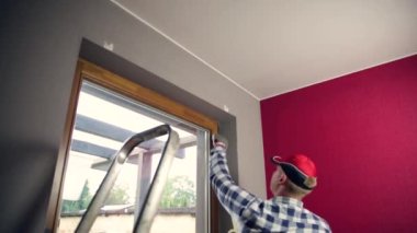 Ev tadilatı. Pencereye boya bandı yapıştıran becerikli bir adam..