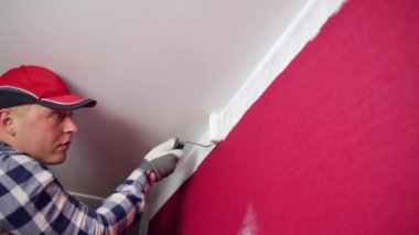 Ev tadilatı. Kırmızı şapkalı bir adam boya silindirli ve fırçalı bir odayı boyuyor..