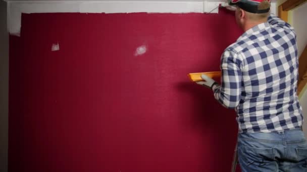ホーム改善 赤い帽子の男が絵の具ローラーで部屋を着色し ブラシをペイント — ストック動画