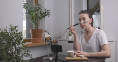 Çevrimiçi cilt bakımı kursuna katılan güzel genç kadınlar akıllı telefonun önüne yeşil kilden bir maske takıyorlar. Güzellik ve cilt bakımı.