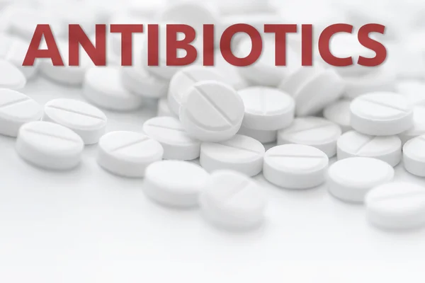 Comprimidos brancos em close-up sobre fundo branco com texto ANTIBIOTI — Fotografia de Stock