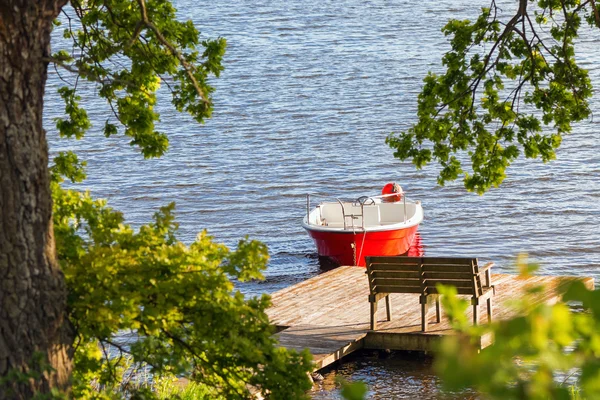 Parked red boat on a lakeside with lush green foliage infront — Stock Photo, Image