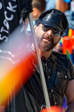 Man with beard in leather and a flag at the Pride parade