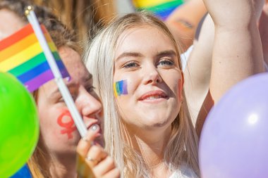 Young blond woman with the rainbow flag painted on cheek at the