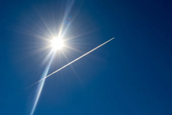 Condensation trail from a aircraft against the bright sun — Stock Fotó