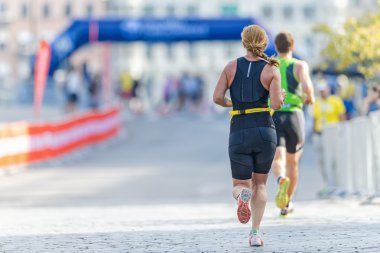 Back of female triathlete running at the cobblestones outside th