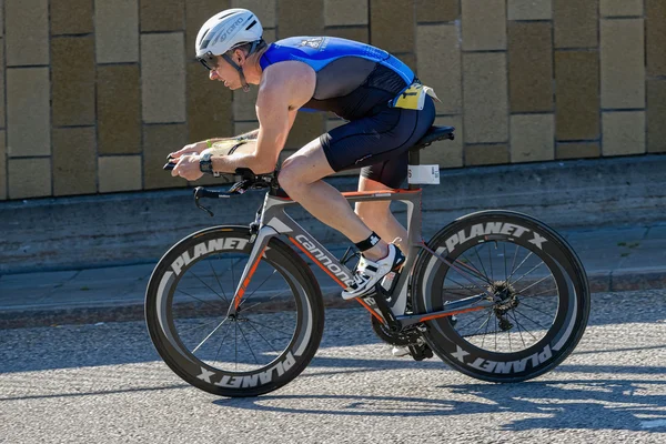 Triathlete cycling with a speedy bike in partial sunlight at the — Stock Photo, Image