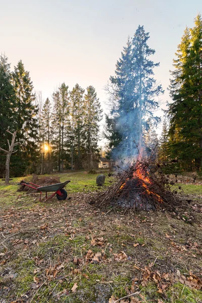 Fuego durante la limpieza del jardín con puesta de sol y una rueda vieja —  Fotos de Stock