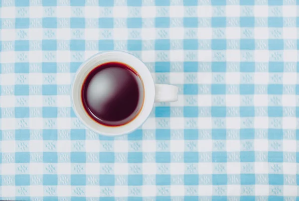 Vista superior da caneca de café preto na toalha de mesa verificada em azul vívido — Fotografia de Stock