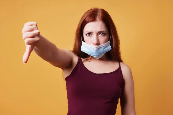 의료용 마스크를 쓴 젊은 여성이 코 아래에 잘못 마스크를 쓰고 제스처로 엄지손가락을 내리는 모습 — 스톡 사진