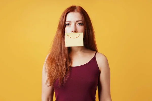 Jeune femme cachant tristesse ou dépression derrière un faux sourire dessiné sur papier — Photo