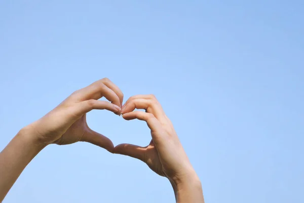 Sinal de mão forma de coração ou gesto de amor contra céu azul claro — Fotografia de Stock