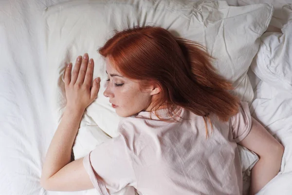 Young woman in bed sleeping on stomach with head on pillow — Stock Photo, Image