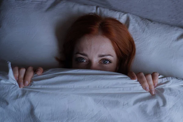 Sleepless woman lying in bed hiding under duvet at night — Stock Photo, Image