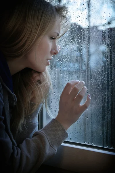 Frau blickt durch Fenster mit Regentropfen — Stockfoto