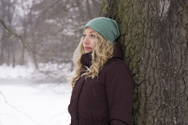 Mulher triste encostada contra a árvore no inverno — Fotografia de Stock