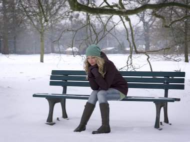 woman sitting alone on park bench in winter