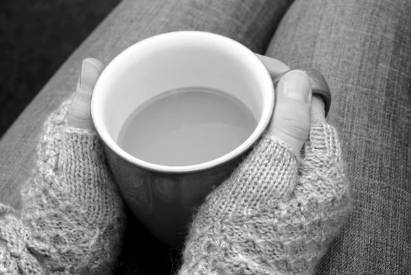 A woman in a cosy jumper holds a cup of tea or coffee on her lap — Stock Photo, Image