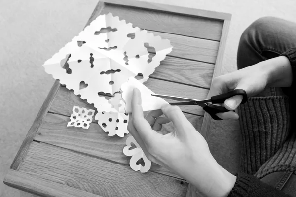 Woman cutting paper into snowflake designs — Stock Photo, Image