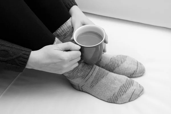 Woman holding a hot drink, wearing warm knitted socks — Stock Photo, Image