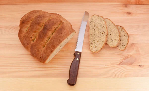 Fresh loaf of bread with a knife and three slices — Stock Photo, Image
