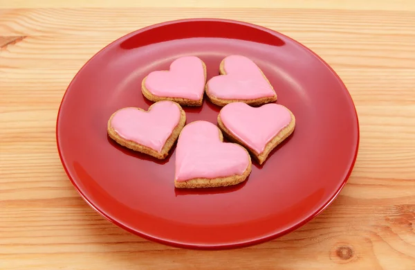 Cinco galletas heladas en forma de corazón en un plato rojo —  Fotos de Stock