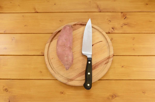 Patata dulce con un cuchillo en una tabla de cortar —  Fotos de Stock