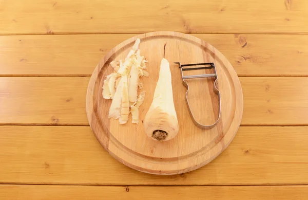 Parsnip descascado com descascador de vegetais em uma tábua de corte — Fotografia de Stock