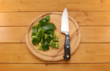 Green pepper being cut with a knife on a chopping board