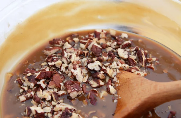 Wooden spoon stirring pecan nuts into pie filling — Stock Photo, Image