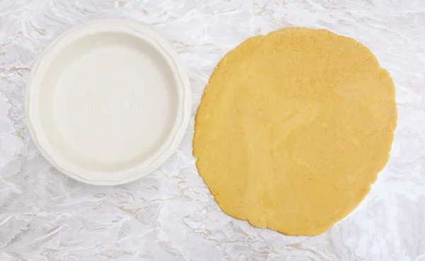 Fresh pastry rolled out in a circle to line pie dish — Stock Photo, Image