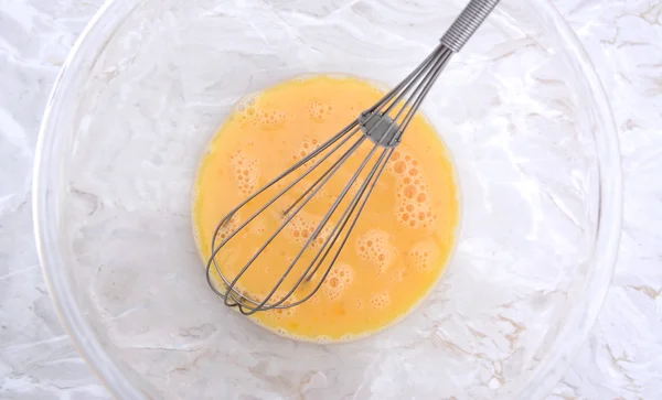 Whisk in a bowl of beaten eggs — Stock Photo, Image