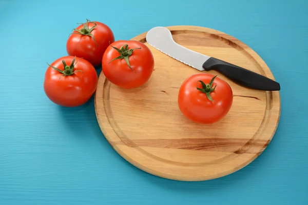 Cuatro tomates en una tabla de cortar con un cuchillo —  Fotos de Stock