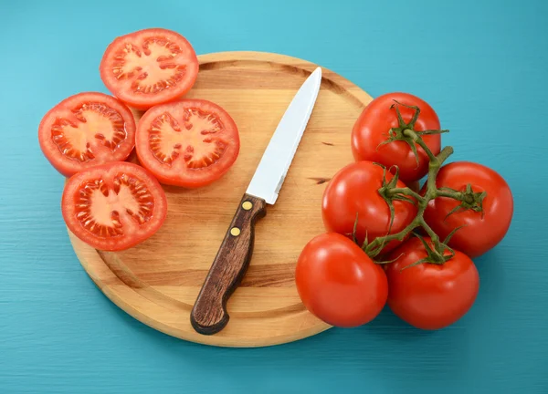 Tomatoes, whole and sliced with knife on wooden board — Stock Photo, Image
