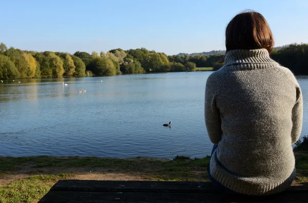 Donna in un maglione caldo seduta da sola vicino a un lago — Foto Stock