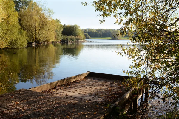 Embarcadero de madera en otoño da a un lago — Foto de Stock