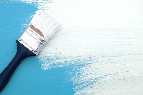 Paintbrush with white paint painting over blue — Stock Photo, Image