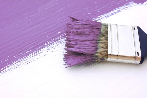 Close-up of paintbrush painting a white board purple