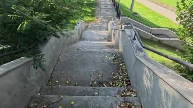 Merdivenlerden inen ve nehir kenarında yürümeye devam eden bir kişinin sakin poziyonu, adımları, hareketleri ve manzaralı kentsel çevreyi birleştiriyor..