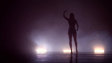 Erotik kız dumanlı arka planda uçan saçlarla seksi dans ediyor.