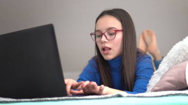 Yatakta dizüstü bilgisayarıyla internette gezinen bir kız.