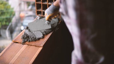 Duvar örmek için tuğla döşeyen bir duvarcı, malasıyla bir yerden harç çıkarıyor.